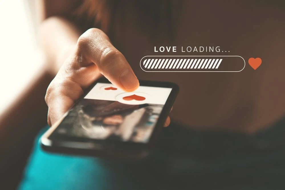 A person uses a smartphone dating app, swiping right on a profile photo. The image includes a "Love Loading..." progress bar with a heart icon.