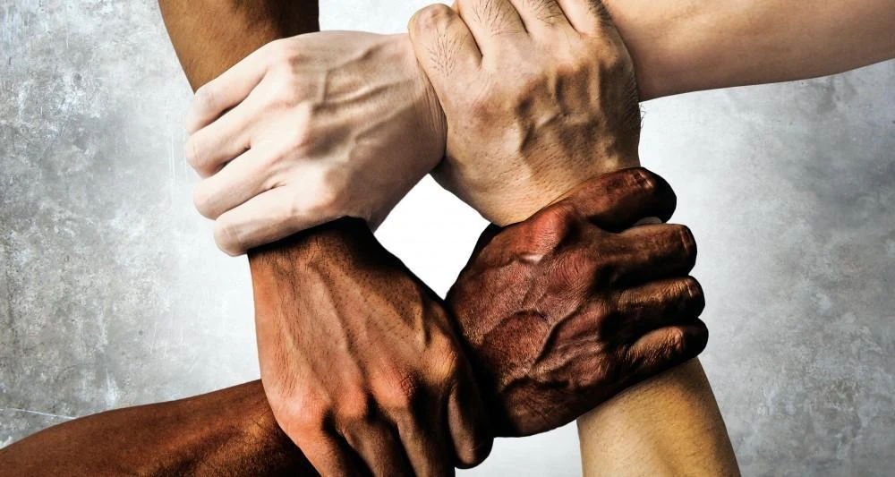 Four hands of different skin tones grasp each other's wrists, forming a square.
