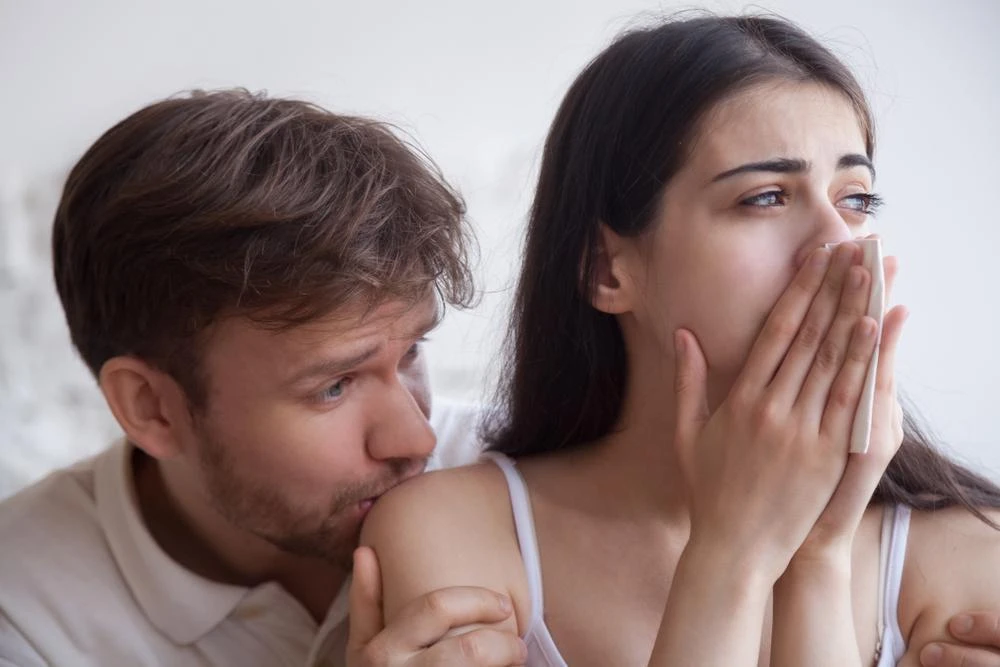 A man comforts a crying woman who is holding a tissue to her face.