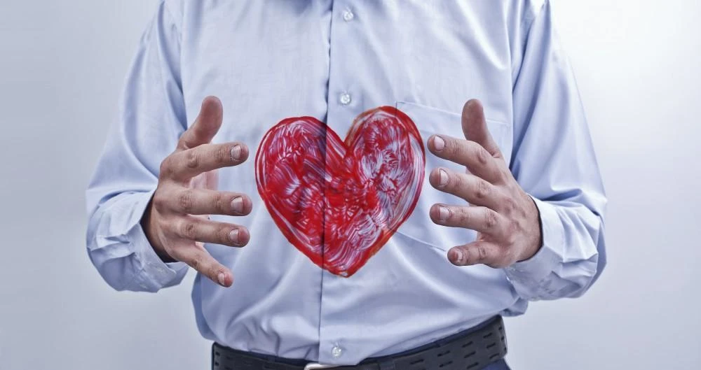 A person in a blue shirt holds a red, abstract heart shape between their hands against a neutral background.