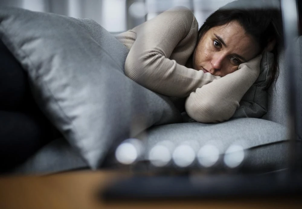 A person lying on a couch, leaning on a cushion, and looking ahead with a serious expression.