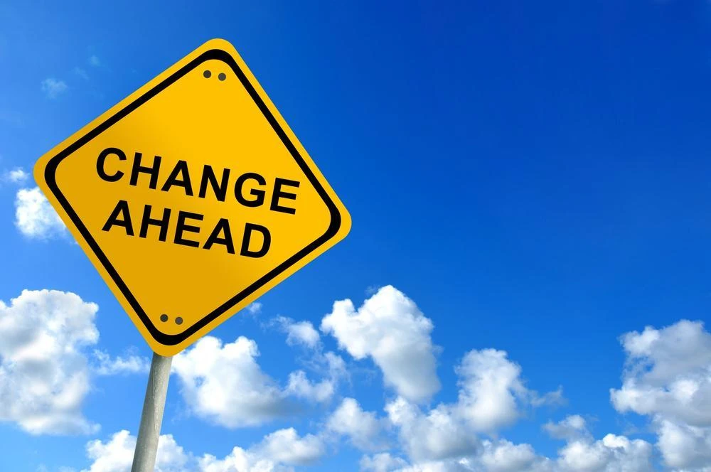 A yellow road sign with the text "Change Ahead" against a background of a blue sky with scattered clouds.