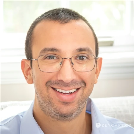 Philip Glickman A person with short dark hair and glasses smiling, wearing a light blue shirt. Providers can be seen in the background through a window with a blurred outdoor view.