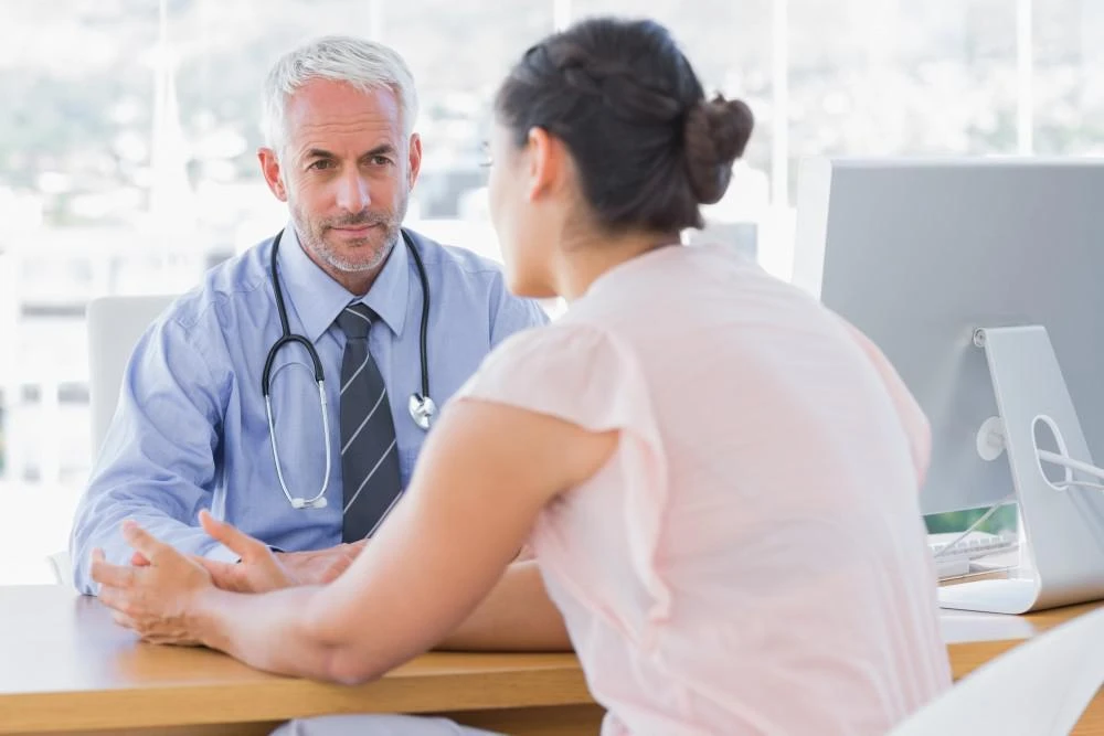 A doctor with a stethoscope around his neck listens intently to a patient during a consultation in a bright office.