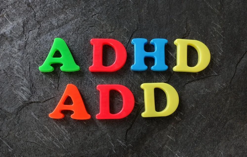Plastic letters on a dark surface spell out "ADHD" in green, red, blue, and yellow and "ADD" in red and yellow.