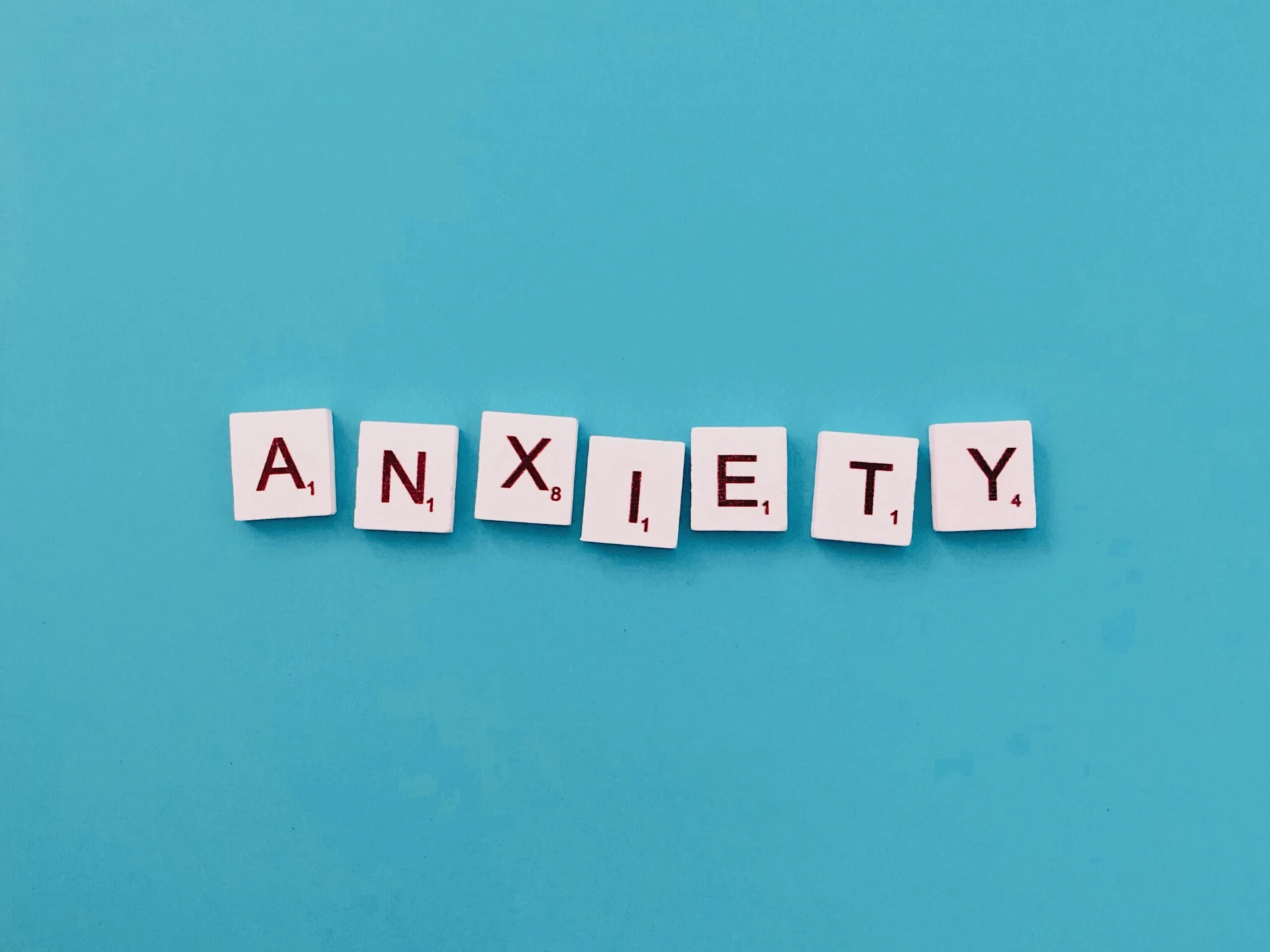 Letter tiles on a blue background spell out the word "ANXIETY.
