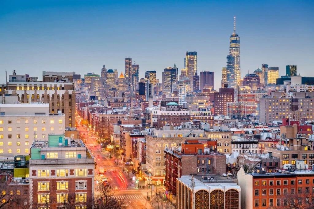 Aerial view of a cityscape at dusk with illuminated skyscrapers in the background and busy streets in the foreground.